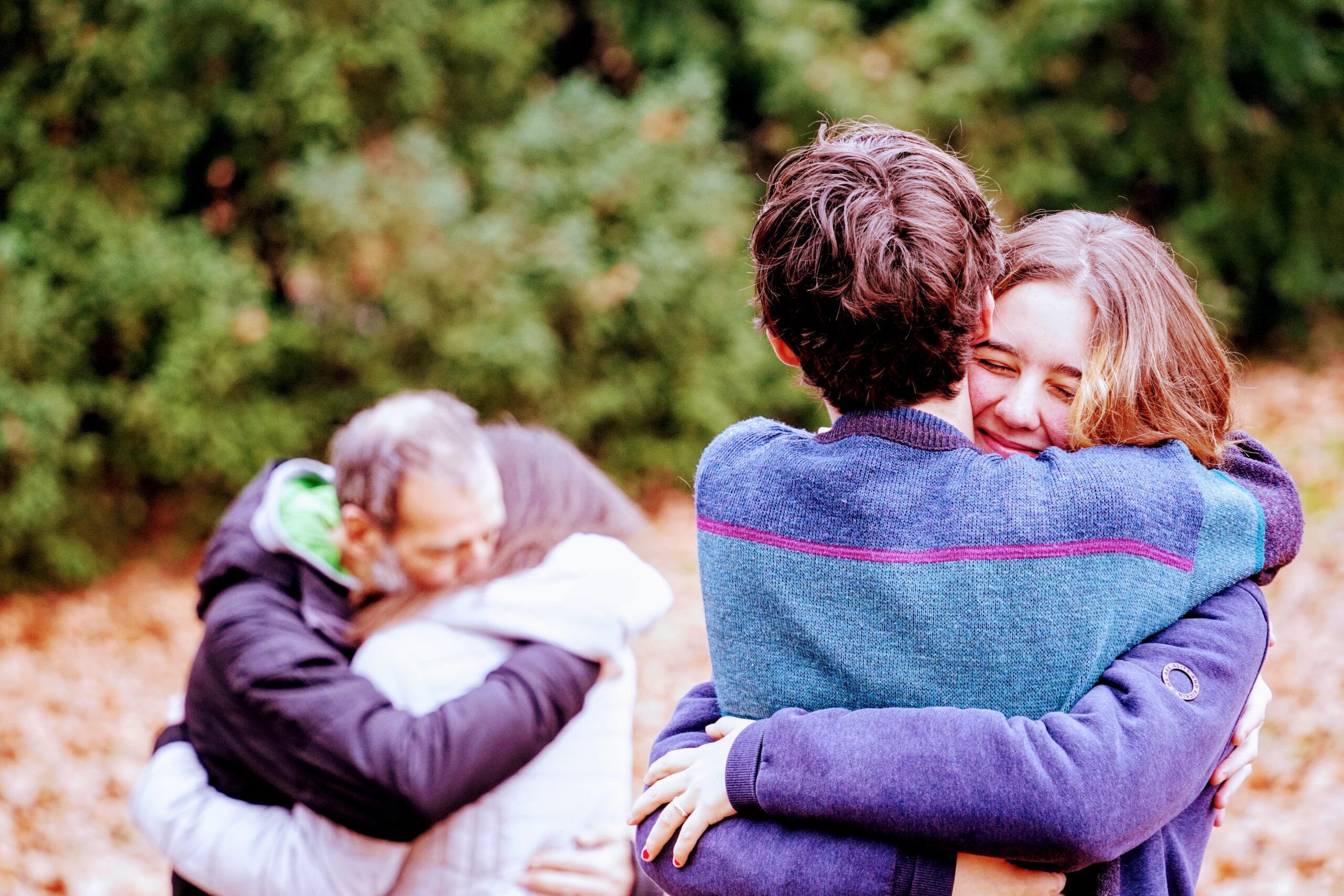 four people hug in the park and smile
