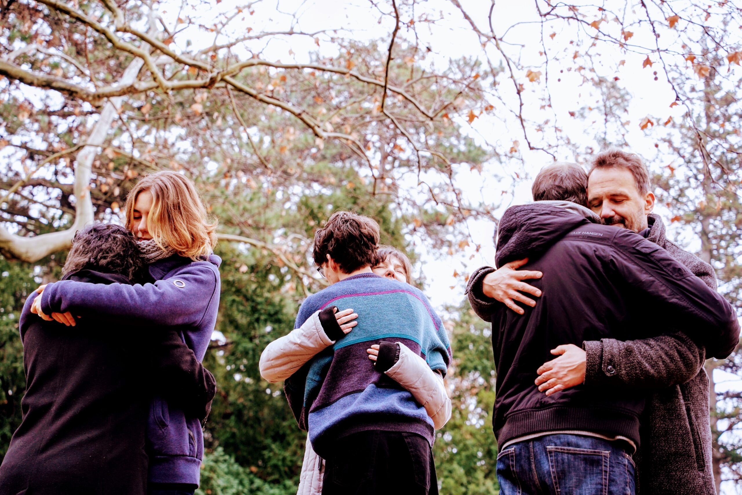 six people hug in the park and smile